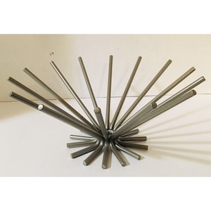 May include: A silver-colored metal fruit bowl with a unique starburst design. The bowl features numerous straight rods radiating outwards from a central point, creating an open, airy structure. The rods are evenly spaced and curved at the base.