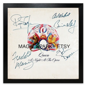 May include: A white vinyl record album cover with the Queen band logo in the center. The album is titled "A Night At The Opera" and features the signatures of all four band members: Freddie Mercury, Brian May, Roger Taylor, and John Deacon.