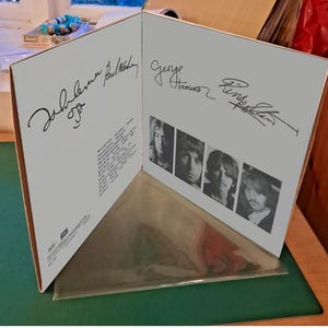 Op de afbeelding: Een openstaande vinyl albumhoes met handtekeningen van John Lennon, Paul McCartney, George Harrison en Ringo Starr. De hoes toont zwart-wit portretten van de bandleden.