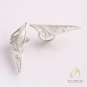 May include: Two silver filigree rings in the shape of a triangle. The rings are delicate and intricate, with a floral design.
