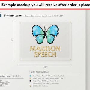 Op de afbeelding: Een mockup van een aangepast bord met de tekst "MADISON SPEECH" in gouden letters op een transparante acryl achtergrond. Het bord is 122 cm breed en 91 cm hoog en heeft een blauw aquarel vlinderontwerp. Het bord is gemonteerd op een witte muur.