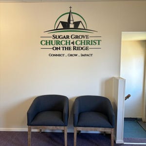 May include: Two dark gray upholstered chairs with light wooden legs positioned in front of a wall featuring the black and green logo and text for Sugar Grove Church of Christ on the Ridge, including the words Connect, Grow, and Impact.