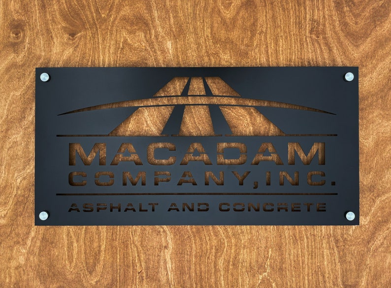 May include: Black metal sign with the text "Macadam Company, Inc. Asphalt and Concrete" and a cut-out design of a highway.
