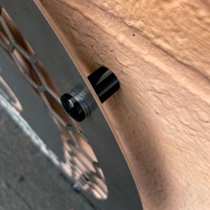 May include: Close-up of a silver metal wall decor with a black metal mounting bracket. The bracket is attached to the back of the decor with a screw.
