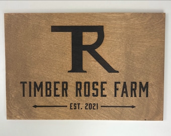 May include: A wooden sign with the text "Timber Rose Farm" and the letter "R" in a large font. The sign also includes the text "Est. 2021" below the farm name.