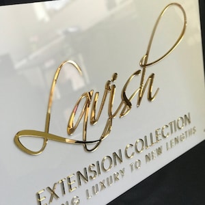 Op de afbeelding: Een wit bord met gouden letters met de tekst "Lavish Extension Collection Taking Luxury to New Lengths".