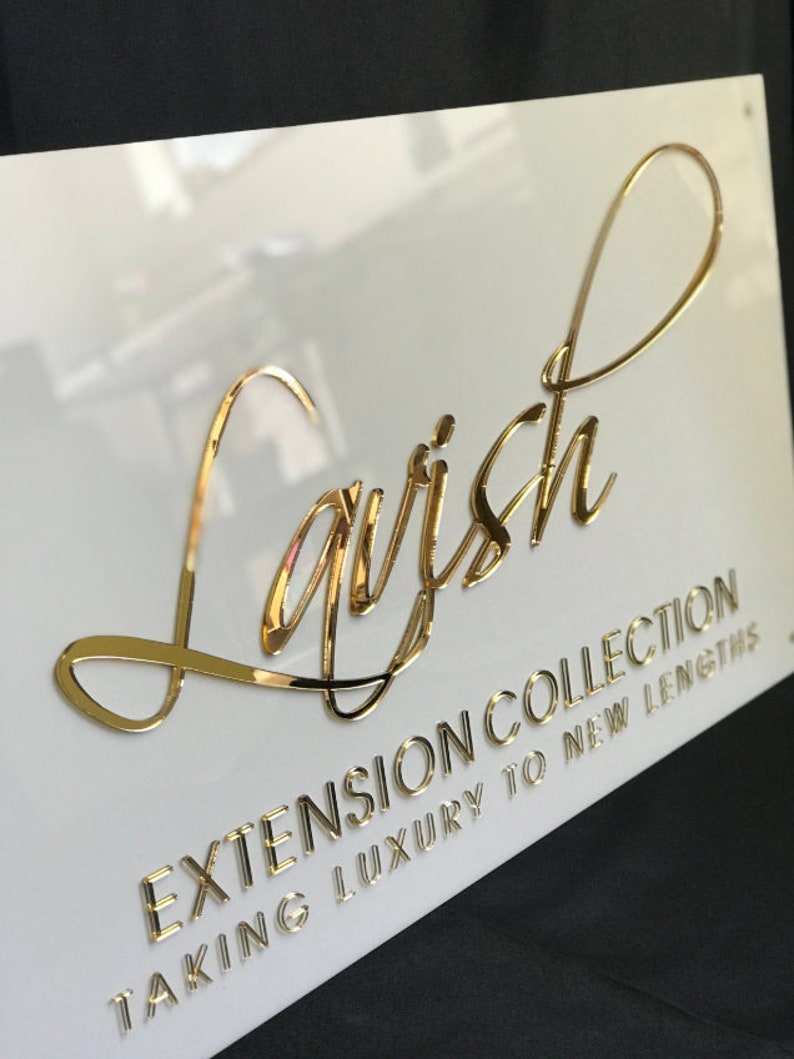 Op de afbeelding: Een wit bord met gouden letters met de tekst "Lavish Extension Collection Taking Luxury to New Lengths".