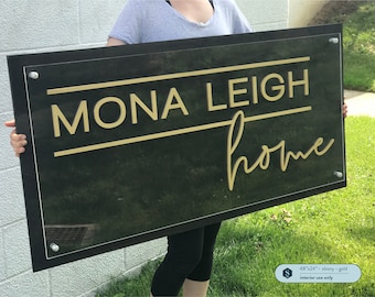 May include: A black acrylic sign with gold lettering that reads "Mona Leigh home". The sign is 48 inches by 24 inches and is for interior use only.