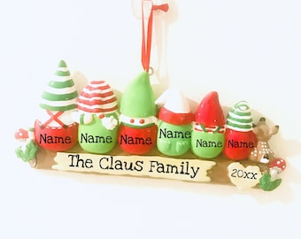 May include: A Christmas ornament featuring a family of six elves with personalized names. The ornament is decorated with green and red colors and includes a reindeer and mushrooms. The text "The Claus Family" and the year "20xx" are also included on the ornament.
