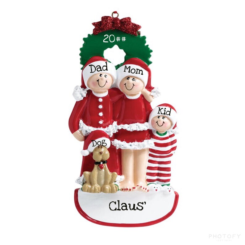 May include: A red and white Christmas ornament featuring a family of four in pajamas, a dog, and a wreath with the text "20##" on it. The family is standing together with the text "Dad", "Mom", "Kid", and "Dog" above them. The ornament also has the text "Claus'" on the bottom.