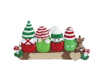 May include: A Christmas ornament featuring four gnomes with red, green, and white outfits and hats. The gnomes are sitting on a brown log with a deer and mushrooms. The ornament is approximately 6 inches long.