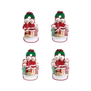 May include: A set of four personalized Christmas ornaments featuring a family of five with a dog. The ornaments are white with a green wreath at the top and a blank space for personalization. The family is dressed in red and white pajamas with green and white striped accents. The dog is wearing a red collar.