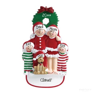May include: A Christmas ornament featuring a family of four in red and white pajamas with a dog. The ornament is decorated with a green wreath and the text "20##", "Dad", "Mom", "Kid", "Kid", "Dog", and "Claus".