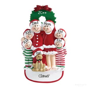 May include: A personalized Christmas ornament featuring a family of six in red and white pajamas, a dog, and a wreath with the text "20##". The ornament has a white base with the text "Claus'" written on it.