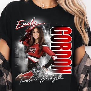 May include: Black t-shirt featuring a cheerleader in a red and white uniform. The shirt has the name "Emily" in script, the word "Gordon" in large red letters, and the text "Twelve Bridges".