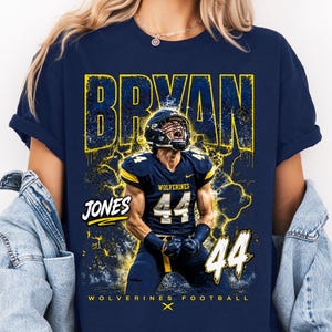 May include: Navy blue t-shirt featuring a football player in a helmet and uniform. The shirt has the name "BRYAN" in yellow, the name "JONES" and the number "44". The text "WOLVERINES FOOTBALL" is also visible.