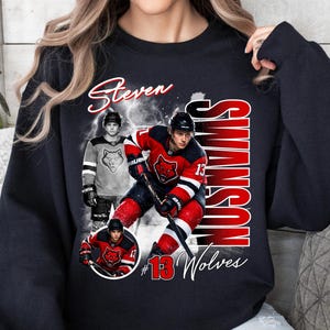 May include: Black sweatshirt featuring a hockey player graphic with the name "Steven Swanson" in white script. The design includes images of the player in action, the number "13", and the word "Wolves" in red and white.