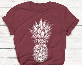Pode incluir: Uma camiseta vinho com um gráfico de abacaxi branco. O abacaxi é desenhado de forma simples e estilizada.