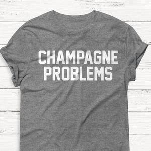 Pu&ograve; includere: Una t-shirt grigia melange con la scritta "CHAMPAGNE PROBLEMS" stampata in bianco.