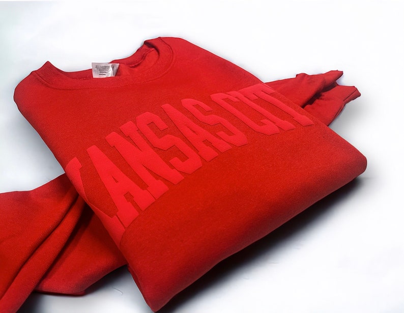 May include: Red sweatshirt with the text "KANSAS CITY" in a bold, raised font.