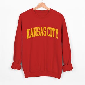 May include: Red sweatshirt with a yellow embroidered "KANSAS CITY" graphic.
