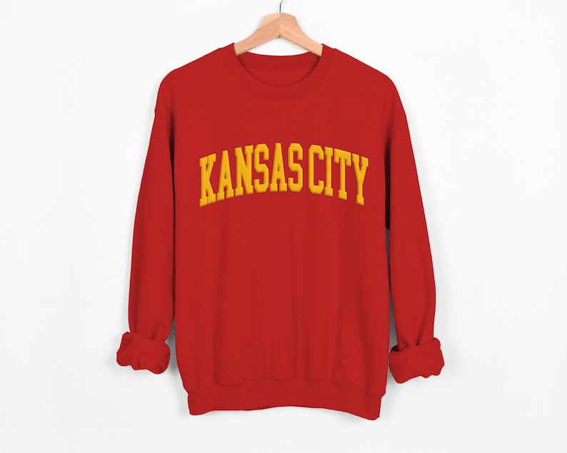 May include: Red sweatshirt with a yellow embroidered "KANSAS CITY" graphic.