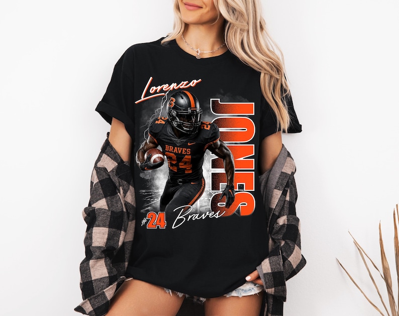 K&ouml;nnte beinhalten: Ein schwarzes T-Shirt mit einer Grafik eines Footballspielers in schwarz-orangem Trikot mit der Nummer 24. Der Text lautet Lorenzo, Jones und #24 Braves. Das Design zeigt einen Football, Blitze und einen rauchigen Hintergrundeffekt.