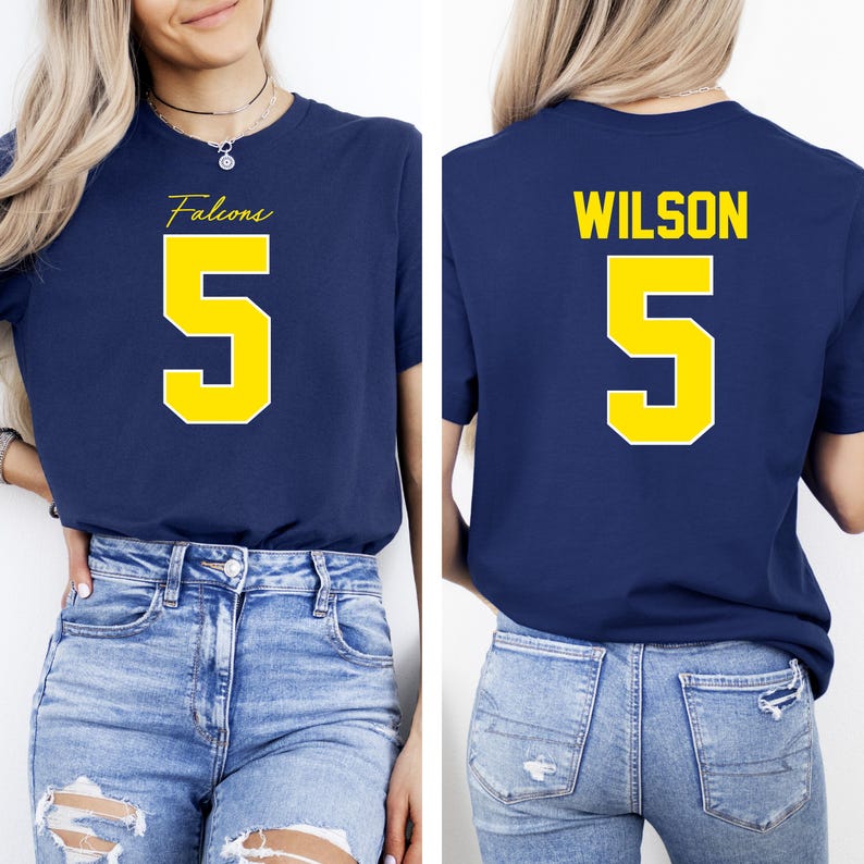 May include: Navy blue t-shirt with the word "Falcons" and the number "5" in yellow. The back of the shirt displays the name "WILSON" and the number "5" in yellow. The shirt is paired with blue jeans.