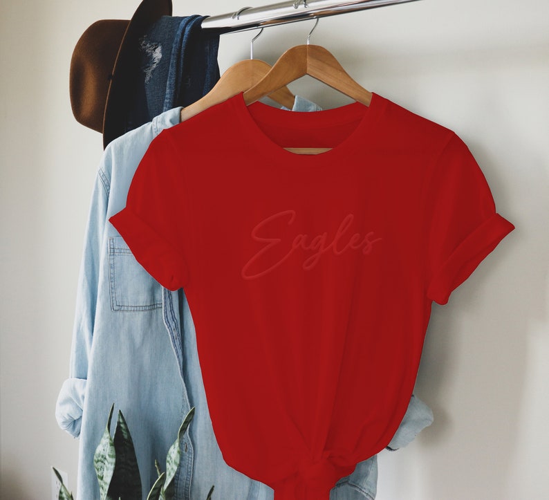 May include: Red short-sleeved t-shirt with the word "Eagles" written in a cursive font.
