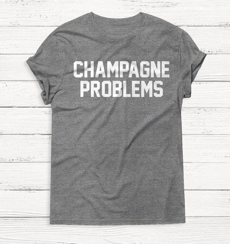 Pu&ograve; includere: Una t-shirt grigia melange con la scritta "CHAMPAGNE PROBLEMS" stampata in bianco.