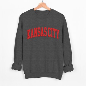 May include: A dark gray sweatshirt with the text "KANSAS CITY" in red embroidered lettering.