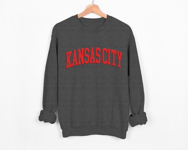 May include: A dark gray sweatshirt with the text "KANSAS CITY" in red embroidered lettering.
