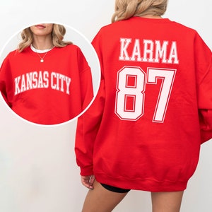 Op de afbeelding: Rood sweatshirt met witte tekst "KARMA 87" op de achterkant.