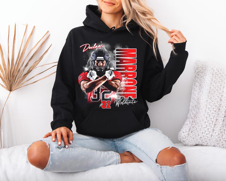 May include: Black hooded sweatshirt featuring a football player graphic. The graphic includes the name "Declan Marrone" and the number "32 Wildcats" in red and white. The player is wearing a helmet and crossed arms.