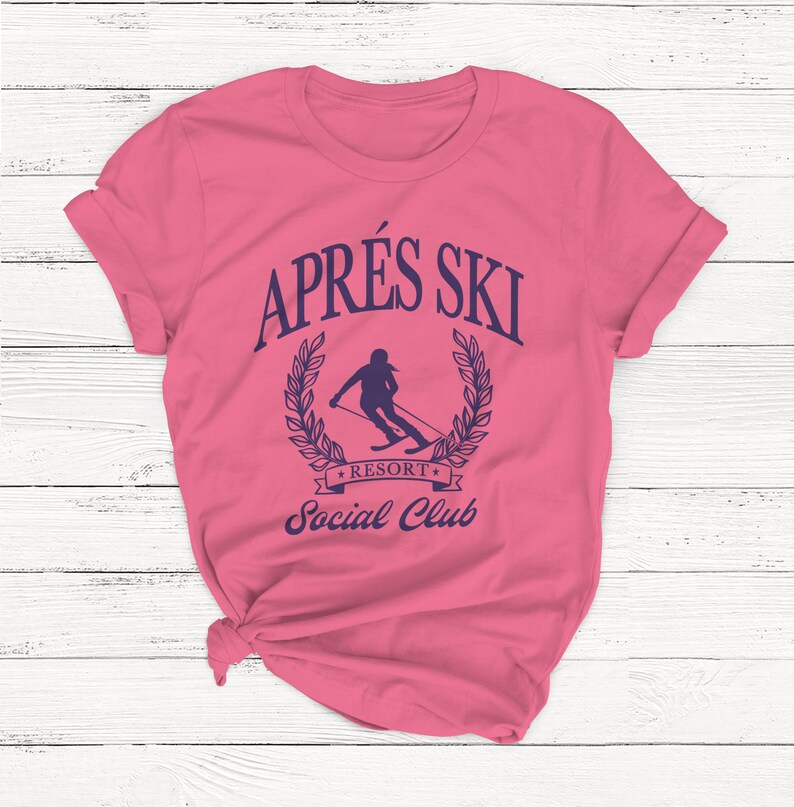 May include: Pink t-shirt with a blue graphic that says "Apr&egrave;s Ski Resort Social Club" and features a silhouette of a skier in a wreath.