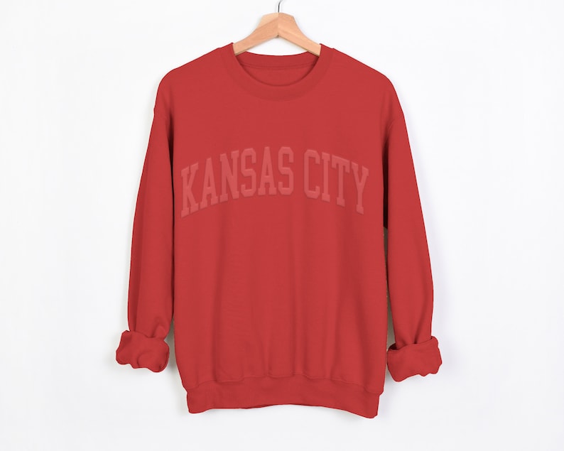 May include: Red sweatshirt with the text "KANSAS CITY" in white letters.