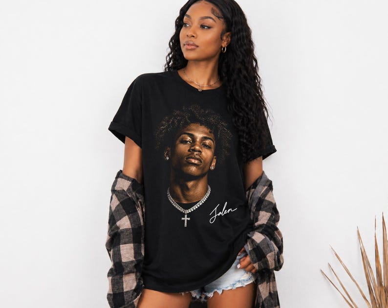 May include: Black t-shirt featuring a portrait of a person with curly hair, a silver chain, and a cross pendant. The name "Jalen" is written in cursive below the portrait. The person is wearing a black and brown plaid shirt.