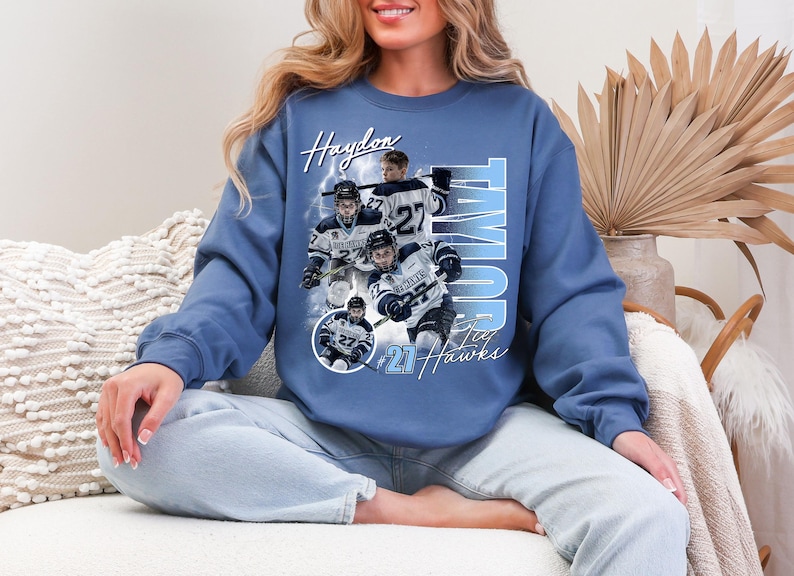 May include: Blue sweatshirt featuring a hockey-themed design. The design includes the name "Haydon" and "Taylor", along with the number "27" and the text "Jay Hawks". The graphic showcases hockey players in action.