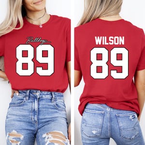 May include: Red t-shirt with the number 89 in white, outlined in black. The front of the shirt has the word "Bulldogs" in cursive above the number. The back of the shirt has the name "WILSON" above the number 89.