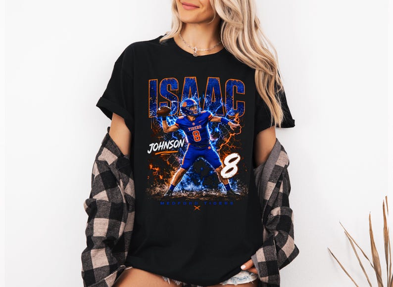 May include: Black t-shirt featuring a football player graphic. The design includes the name "ISAAC" in blue and orange, the name "JOHNSON", the number "8", and the words "MEMPHIS TIGERS". The player is in a blue uniform.