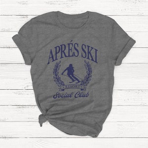 May include: Gray t-shirt with a blue graphic that says "Apr&egrave;s Ski Resort Social Club". The graphic features a skier in a wreath.