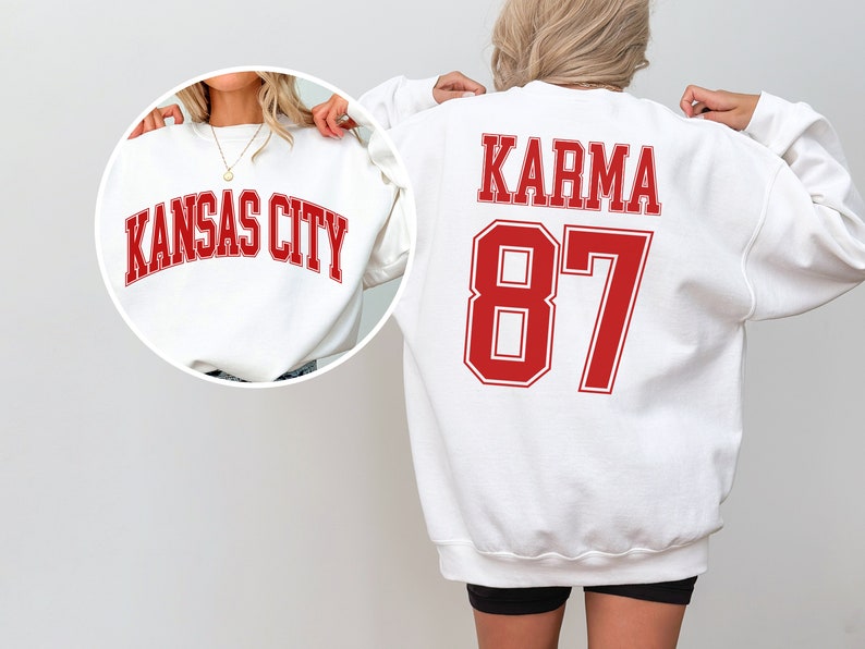 Op de afbeelding: Twee witte sweatshirts met rode letters. E&eacute;n sweatshirt zegt "Kansas City" en de andere zegt "Karma 87".