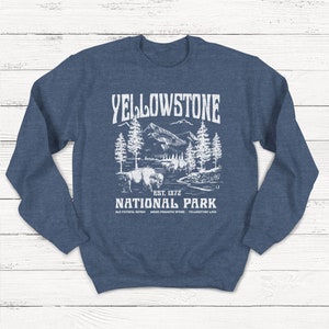 May include: A navy blue sweatshirt with a white graphic design of a mountain landscape, a bison, and the text "Yellowstone National Park Est. 1872 Old Faithful Geyser Grand Prismatic Spring Yellowstone Lake".