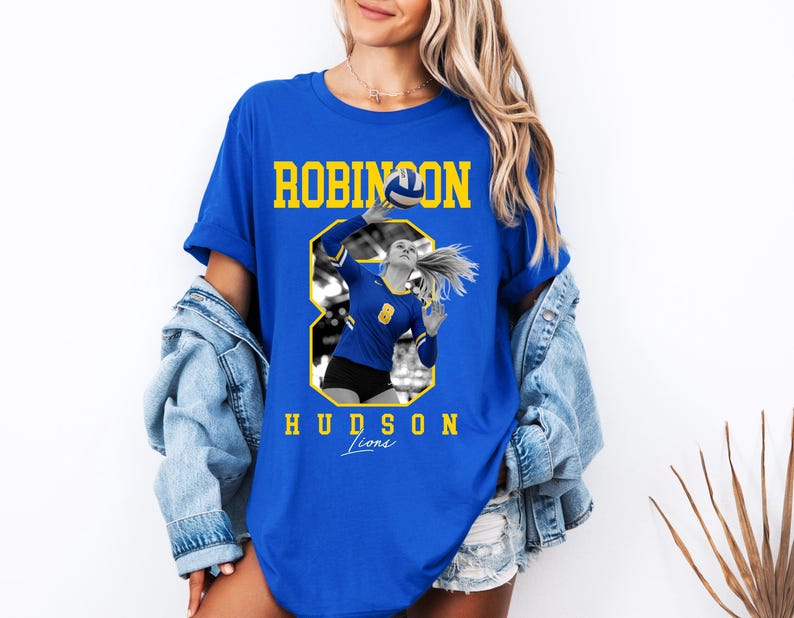 May include: Royal blue t-shirt featuring a volleyball player in action, with the text "ROBINSON HUDSON Lions" in yellow. The graphic includes a volleyball and the number 8. The shirt is a casual, sporty style.