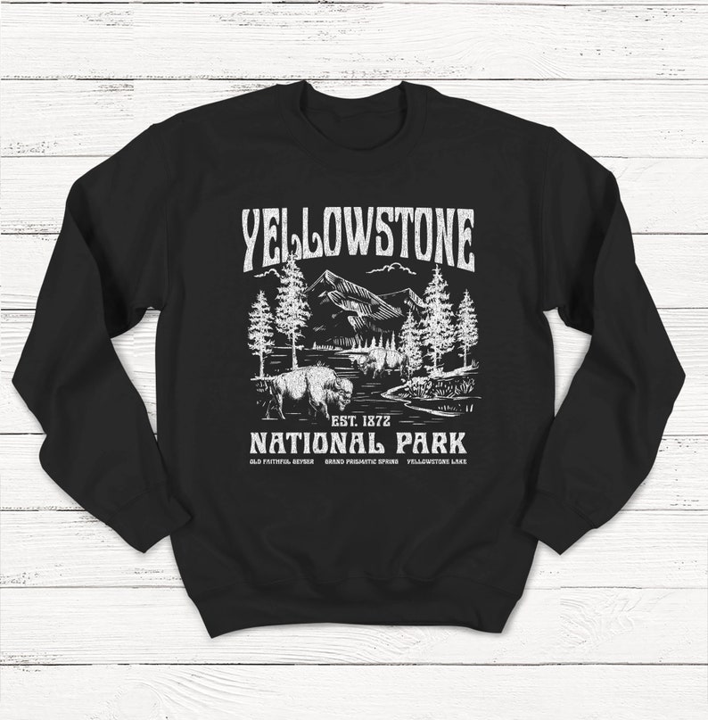 May include: Black sweatshirt with a white graphic design of a mountain landscape with trees and a bison. The text "Yellowstone National Park" is printed in white with the words "Est. 1872" and "Old Faithful, Geyser, Grand Prismatic Spring, Yellowstone Lake" printed below.