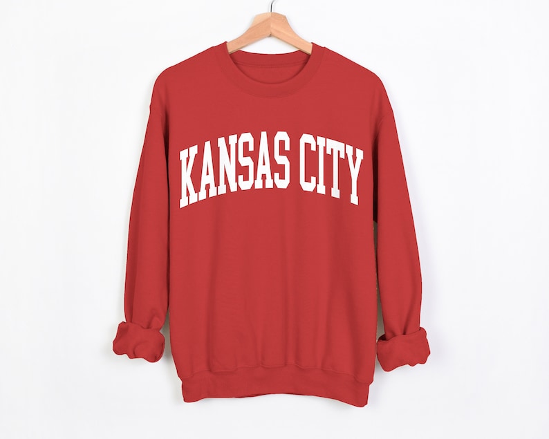 May include: Red sweatshirt with white text that reads "KANSAS CITY" in a collegiate font.