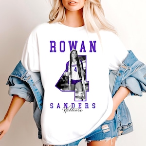 May include: White t-shirt with the name "ROWAN" in purple block letters. A photo of a volleyball player in a purple and white uniform is integrated into a large purple number "4". The name "SANDERS Wildcats" is printed below the number.