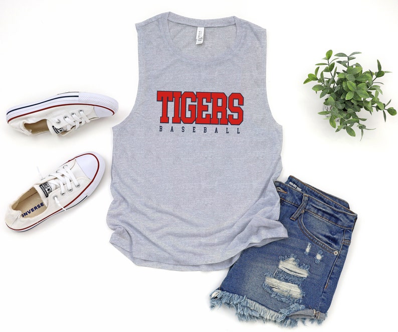 May include: Gray sleeveless tank top with the word "TIGERS" in red and "BASEBALL" in blue underneath. The tank top is laying on a white surface with a pair of white sneakers and denim shorts.
