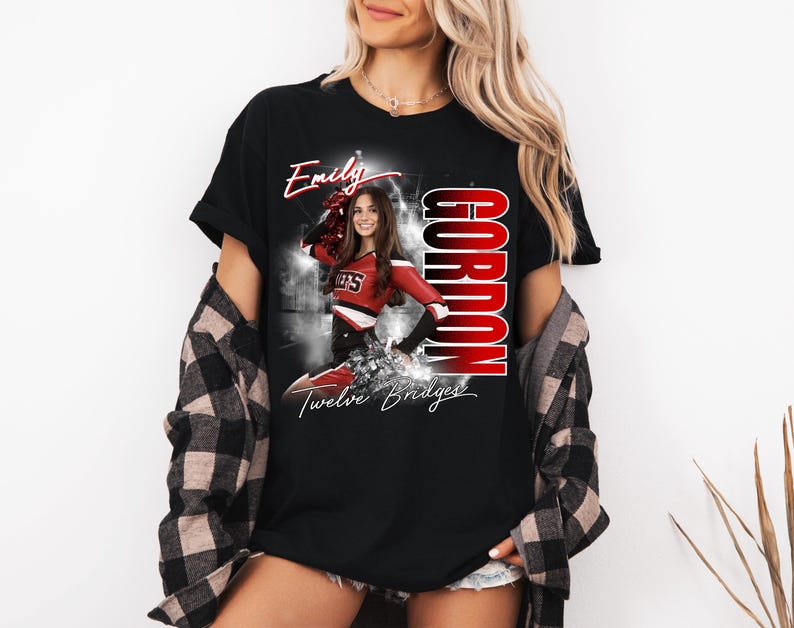 May include: Black t-shirt featuring a cheerleader in a red and white uniform. The shirt has the name "Emily" in script, the word "Gordon" in large red letters, and the text "Twelve Bridges".