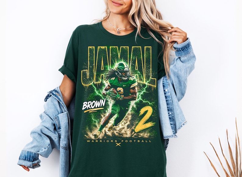 May include: Dark green t-shirt featuring a football player graphic with the name "JAMAL" and "BROWN" in yellow. The number "2" is also in yellow. The words "WARRIORS FOOTBALL" are at the bottom.